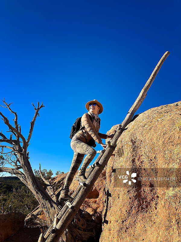 女人攀登梯子，位于新墨西哥州班德利尔国家纪念碑的Tsankawi小径图片素材