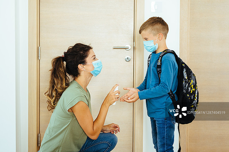 单亲妈妈给小男孩的手喷洒洗手液，两人都戴着口罩图片素材