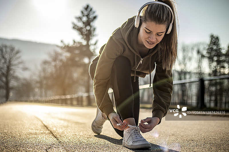 特写：女人系鞋带 - 一个美丽的健康女人独自在赛道混凝土部分的大自然中跑步 - 一个年轻的女运动员在外面慢跑图片素材