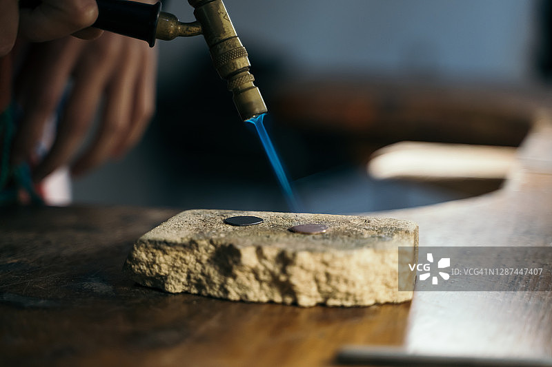 在珠宝工作室里，用喷灯在石头上熔化圆形金属块的人图片素材