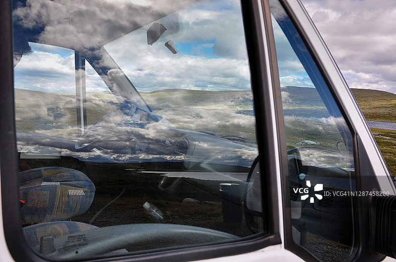 房车窗户中多云天空的倒影，汽车停在山地景观中图片素材