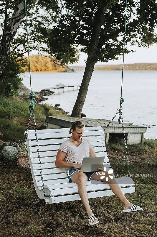 男人在花园秋千上使用笔记本电脑图片素材