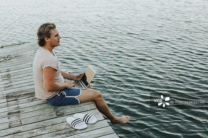 男人坐在码头上使用笔记本电脑图片素材
