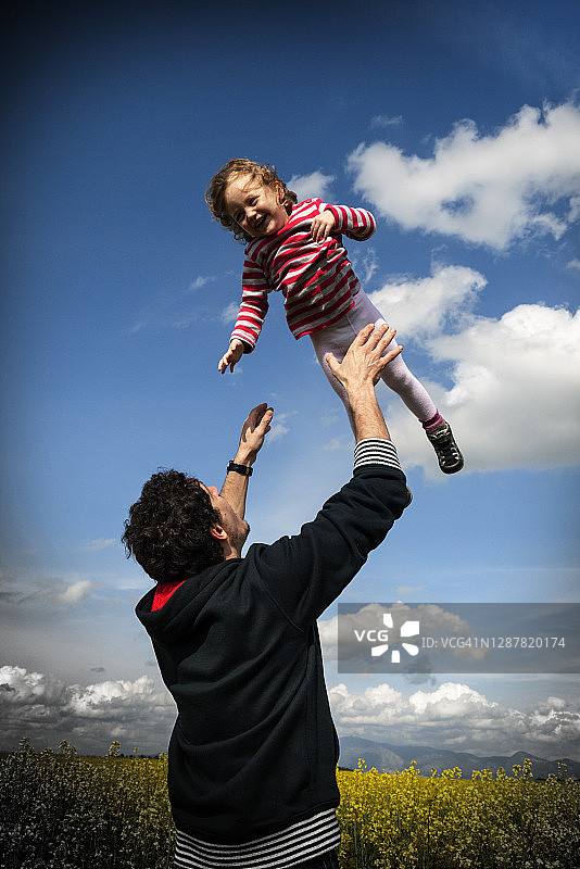 父亲站在田野里，将女儿抛向空中图片素材