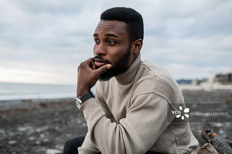 坐在海滩上望着大海的黑发络腮胡青年男子图片素材