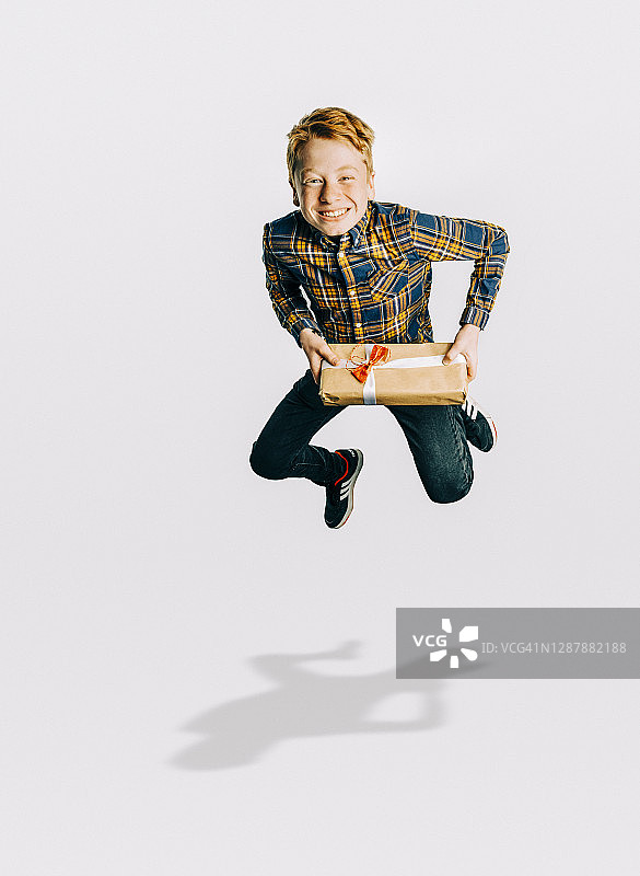 兴奋地拿着圣诞礼物的男孩跳跃图片素材