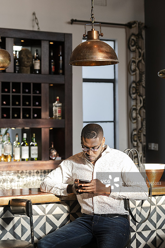 在酒吧使用手机的时尚非洲裔男性图片素材