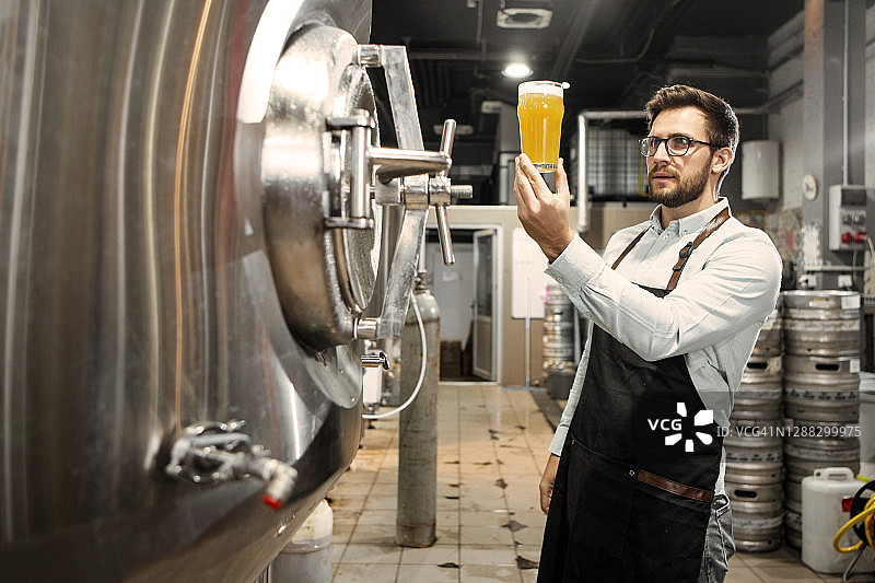 在啤酒厂检查质量的持啤酒杯的年轻人图片素材