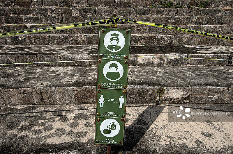 墨西哥尤卡坦乌斯马尔遗址金字塔前的西班牙语新冠疫情安全标牌和警戒带图片素材