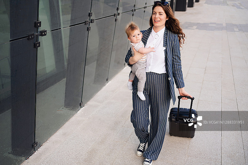 快乐的女人抱着宝宝拖着行李箱图片素材