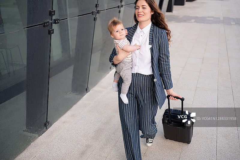 自信的年轻母亲抱着婴儿拖着行李箱图片素材