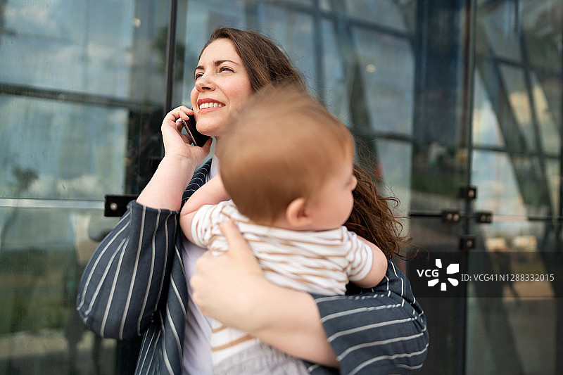 年轻母亲在户外抱着儿子打电话图片素材