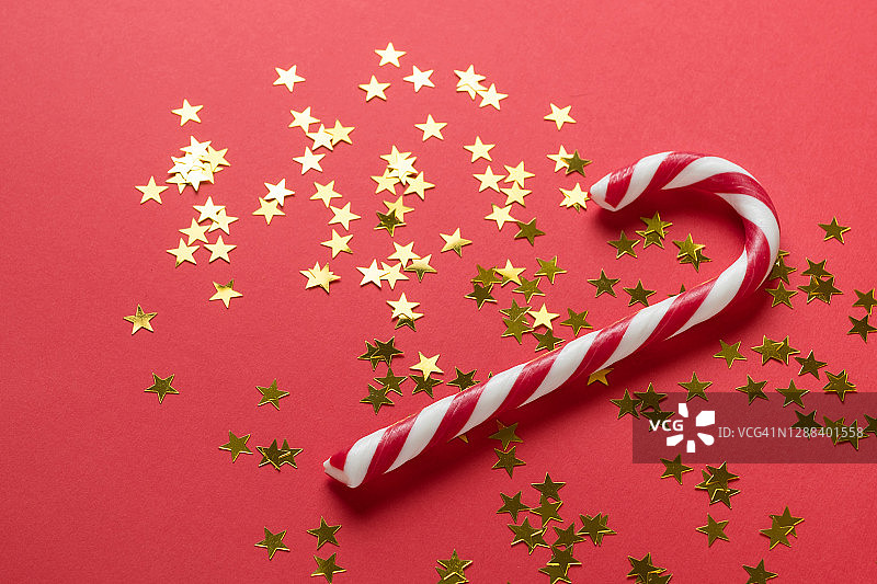 圣诞条纹糖果和金色星星纸屑在美丽的红色节日背景上散落图片素材