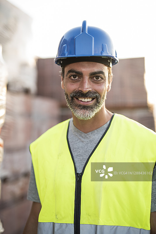 拉丁裔男人在建筑工地，戴着头盔和安全背心的工人肖像，面带微笑图片素材