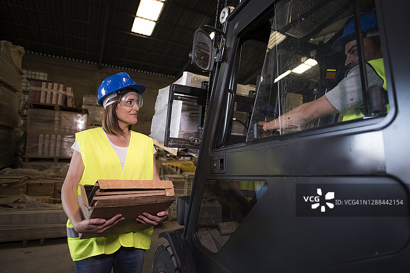 运输建筑公司：男女工人在堆积的材料背景下亲切交谈工作和材料的分解图片素材