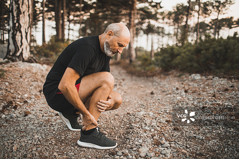 户外跑步中小腿肌肉受伤，年长的男人手扶膝盖，感到疼痛，韧带或骨膜扭伤问题图片素材