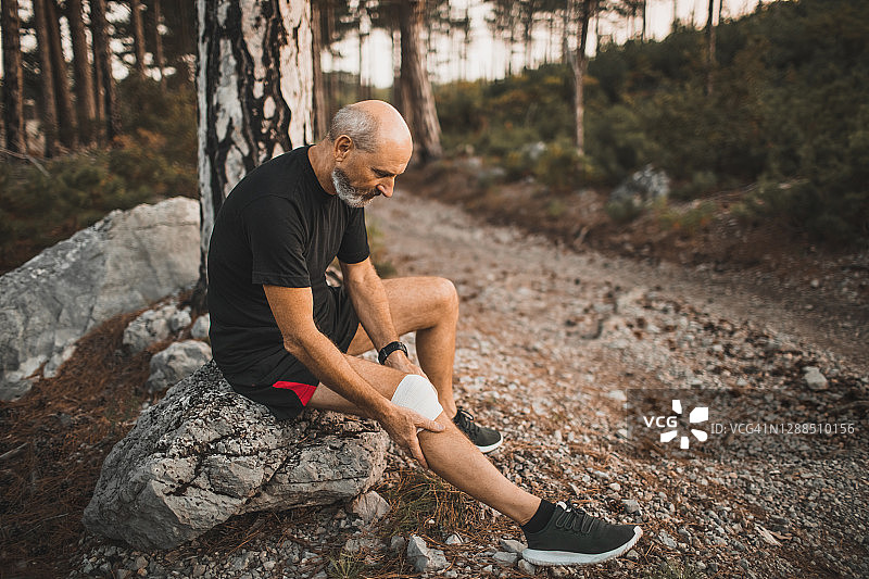 老年男性跑步者包扎受伤的膝盖，户外跑步时腿部受伤，用于扭伤韧带或肌腱的急救图片素材