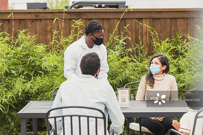 一家三口在露台餐桌旁向服务员点餐图片素材