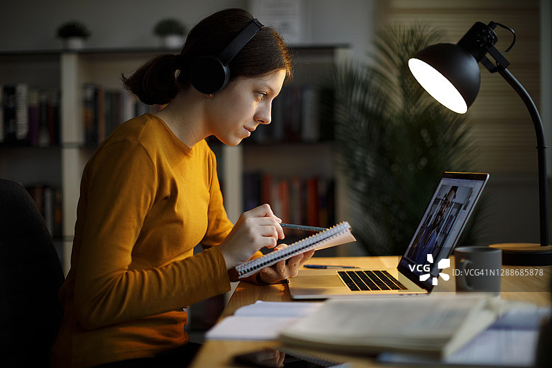 在家用笔记本电脑学习的微笑少女，戴着无线耳机图片素材