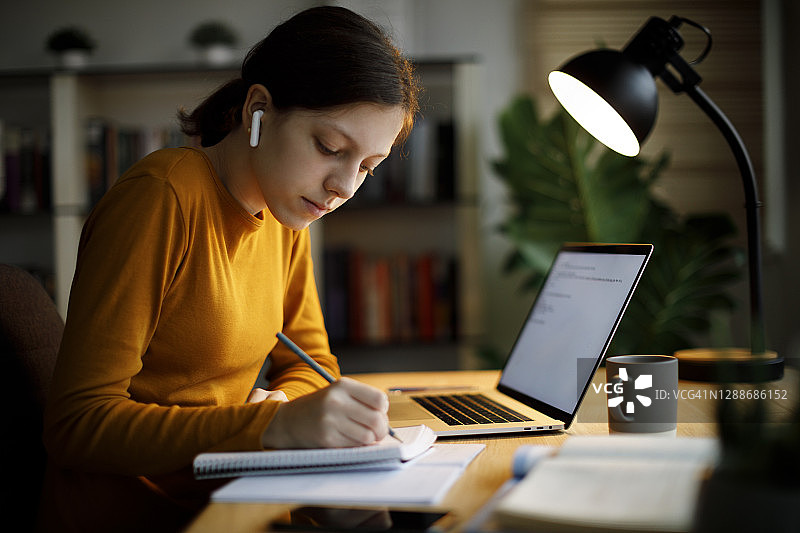 戴着蓝牙耳机在家用笔记本电脑学习的少女图片素材