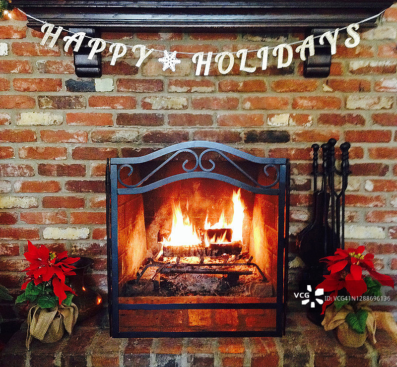 砖砌壁炉中燃木火焰，圣诞装饰品和节日快乐标志悬挂在上方图片素材