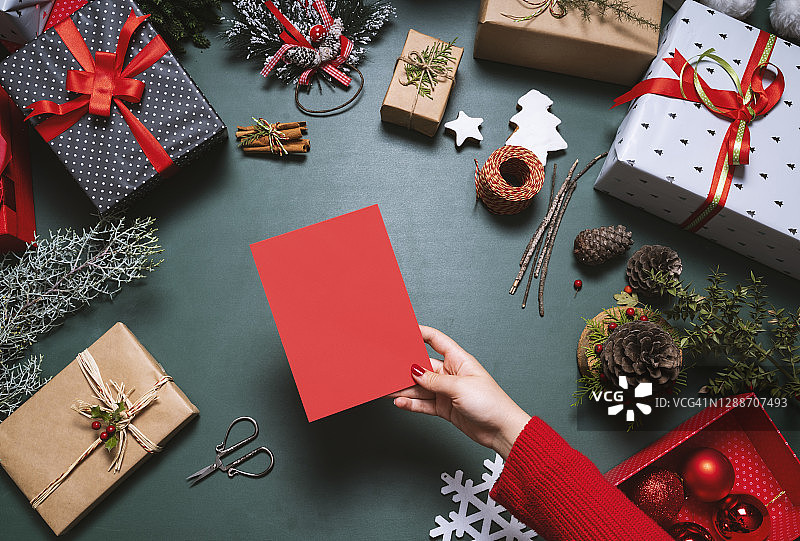 手持圣诞贺卡，背景为圣诞礼物和装饰品图片素材