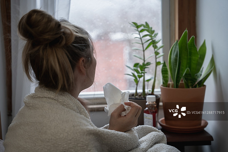 年轻女子生病在家，望着雨天窗外图片素材
