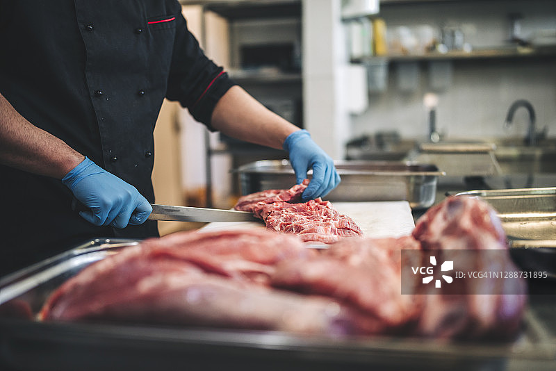 男屠夫在餐厅厨房用锋利的刀切割生肉图片素材
