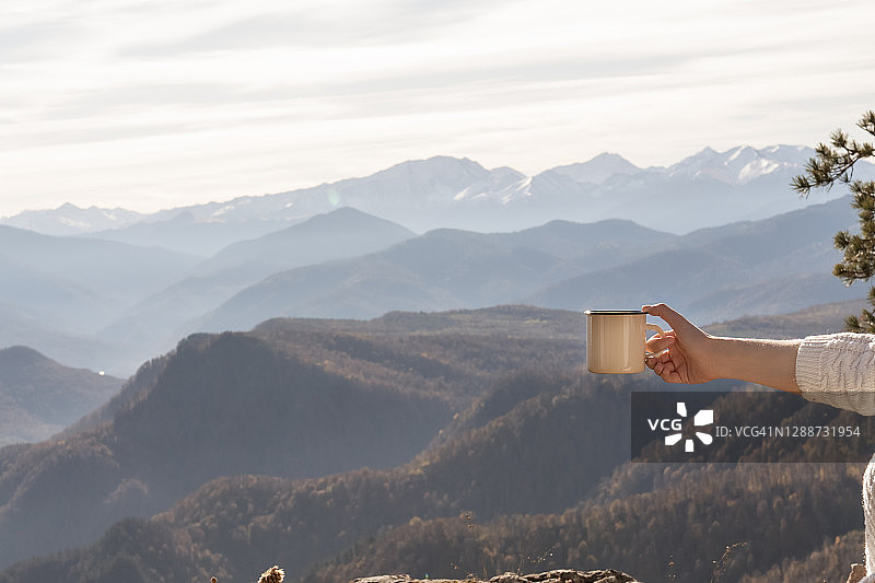 手持白色搪瓷露营杯样机，背景为河景。用于设计推广的空杯子模型图片素材