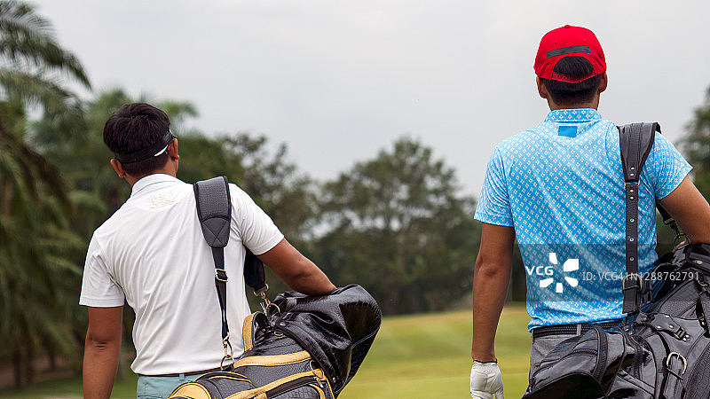 亚洲男人和朋友从高尔夫球车上拿起高尔夫球包，走到发球区开始高尔夫比赛图片素材