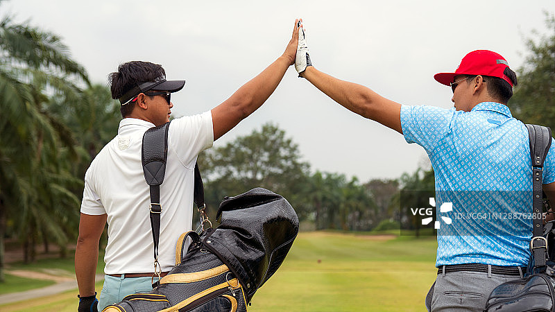 亚洲男人和朋友从高尔夫球车上取下高尔夫球包，朋友们在高尔夫球场上击掌图片素材