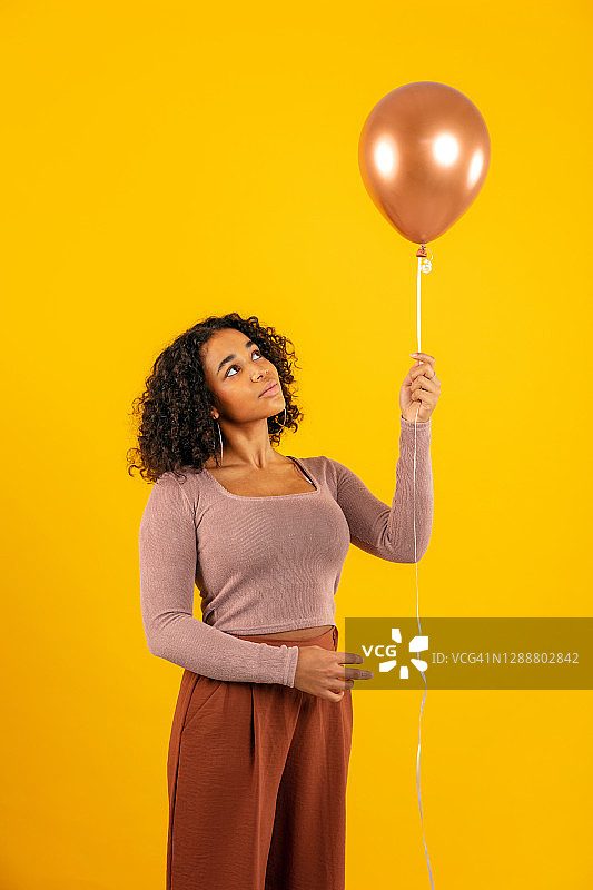 站在黄色背景前看气球的沉思女人图片素材
