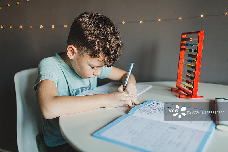 一个学龄儿童坐在家里的桌子旁，完成一项作业，写着家庭教育图片素材