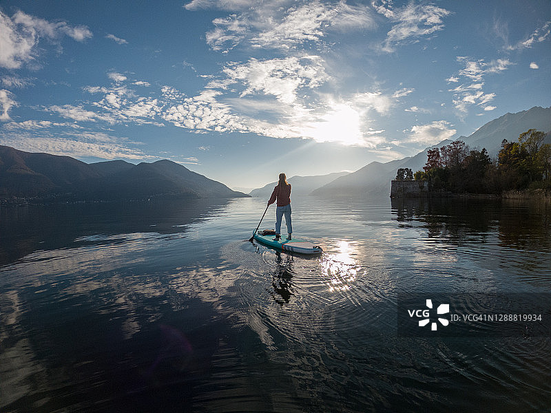女人日落时分在湖上划立式桨板图片素材