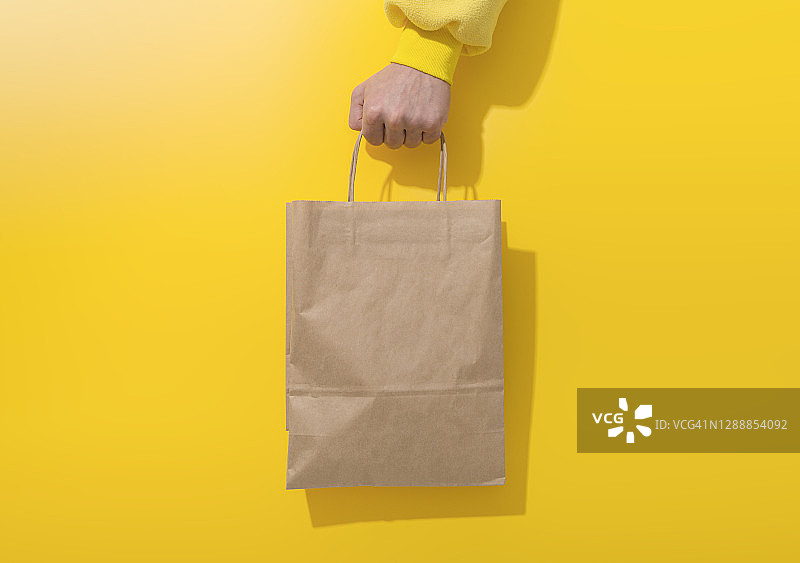 手持黄色背景上的纸袋图片素材