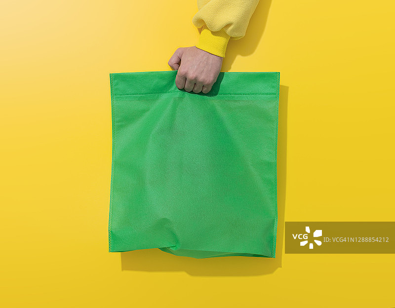 手持黄色背景上的绿色棉布袋图片素材