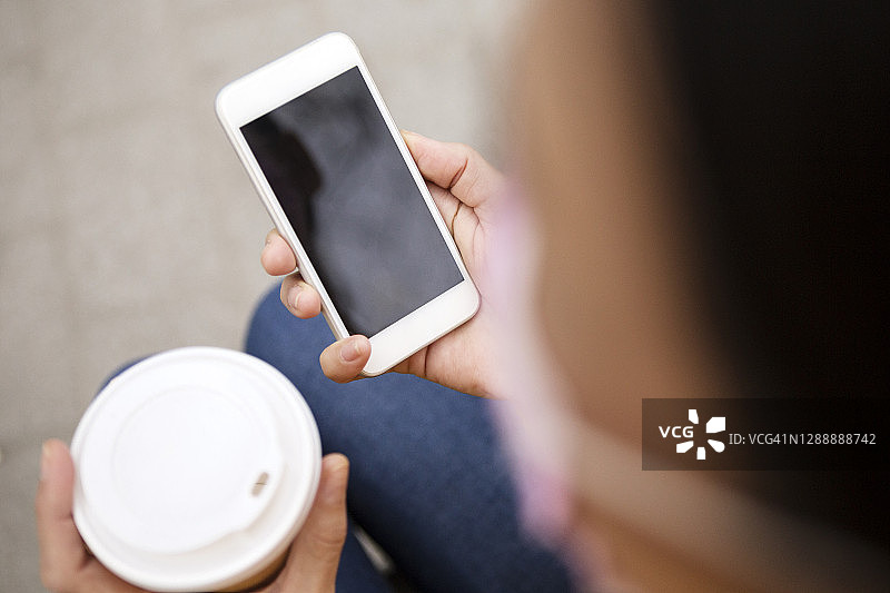 年轻女子手拿咖啡杯看空白智能手机，有复制空间图片素材