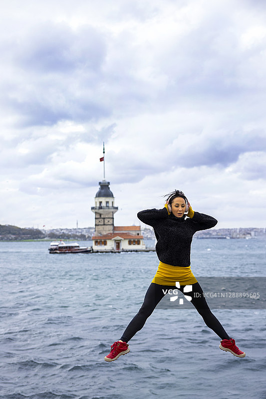 年轻女人在伊斯坦布尔少女塔前听音乐跳跃图片素材