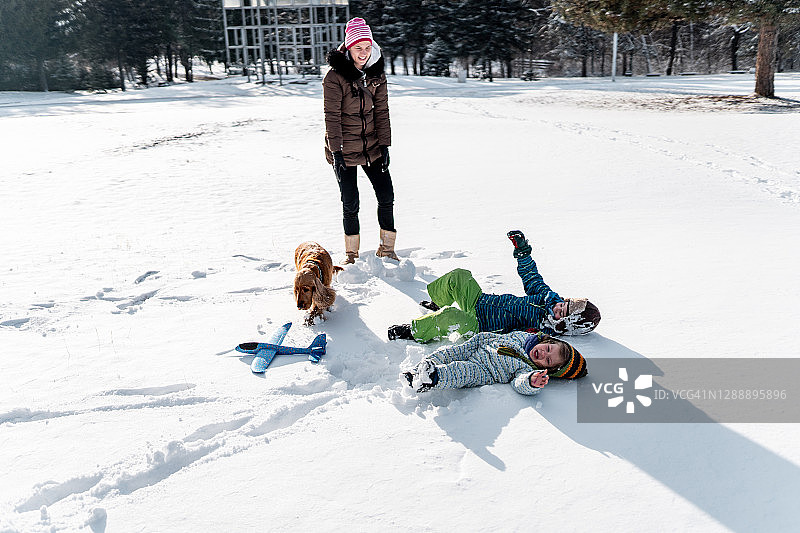年轻母亲和两个孩子及宠物狗在雪地里玩耍图片素材