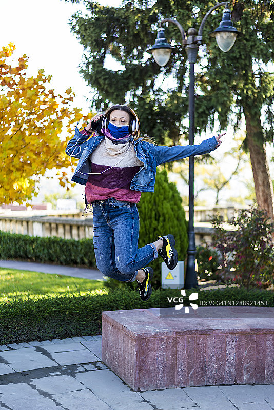 年轻女子戴着口罩在公园里用手机听音乐图片素材
