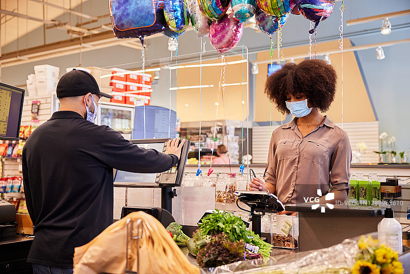 戴着口罩在有机玻璃保护的收银台前购买杂货的年轻女人图片素材