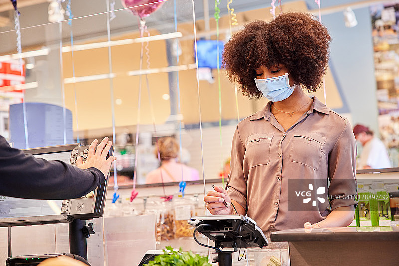 戴着口罩在有机玻璃保护的收银台付款的女人图片素材