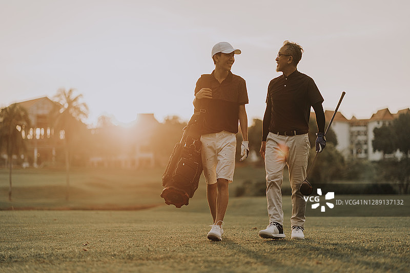中国父子在高尔夫球场日落时分愉快交谈，笑容满面图片素材