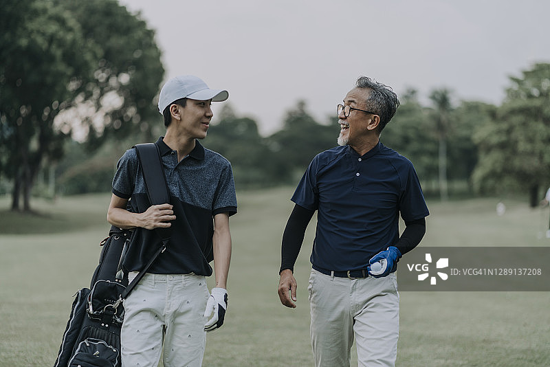 中国父子在高尔夫球场散步交谈图片素材
