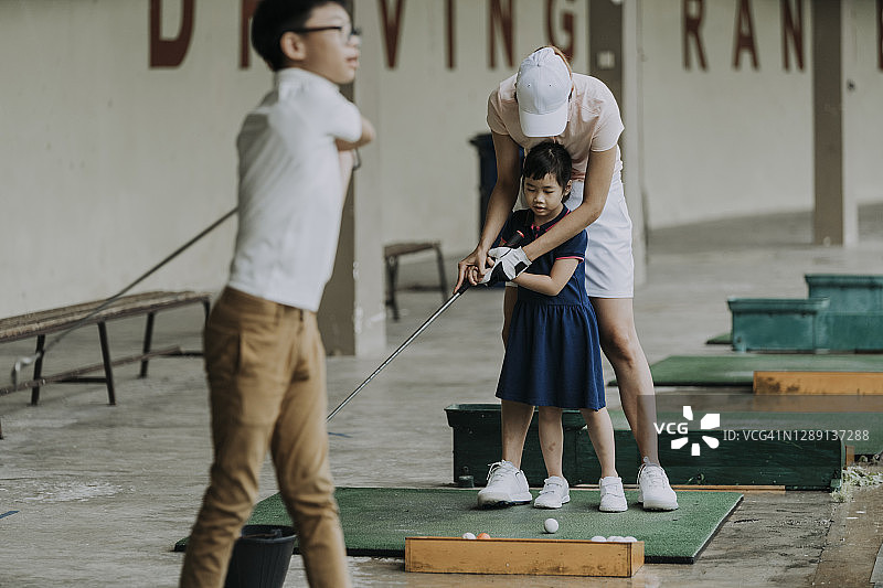 亚洲华裔高尔夫球手母亲在练习场教女儿打高尔夫图片素材