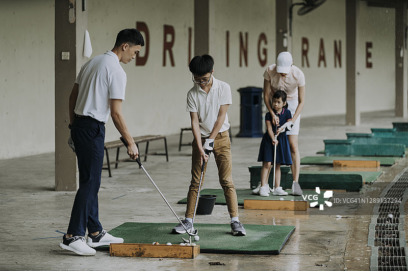 亚洲华人成熟男子高尔夫教练教年轻男学生在练习场打高尔夫图片素材