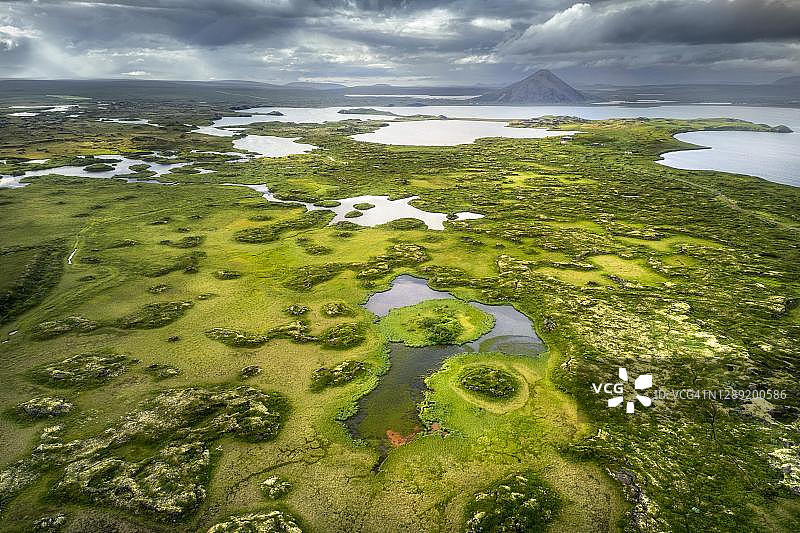 绿色植被和小型湖泊岛屿的精细景观,火山锥和云层后,米湖火山,斯库图斯塔迪尔,冰岛东北部图片素材