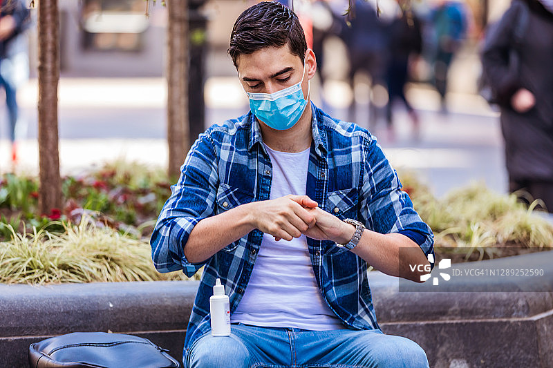 戴着口罩的年轻男子用消毒剂清洁他的手图片素材