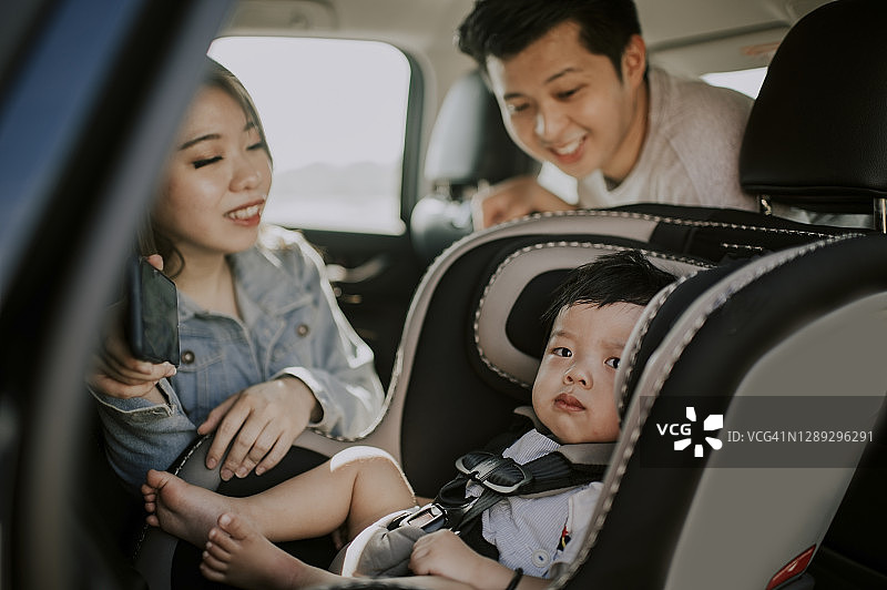 亚洲中国婴儿男孩坐在汽车后座的婴儿座椅上，与父母外出图片素材