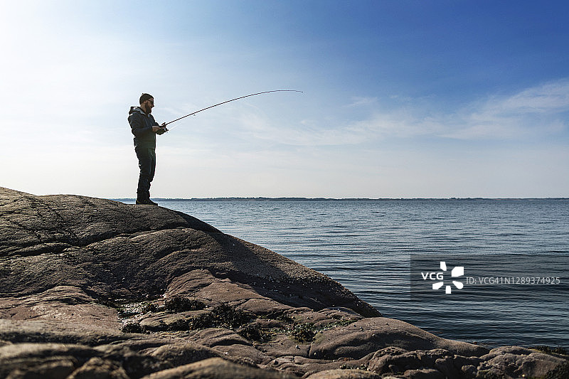 男人在海边的岩石上用钓竿钓鱼图片素材
